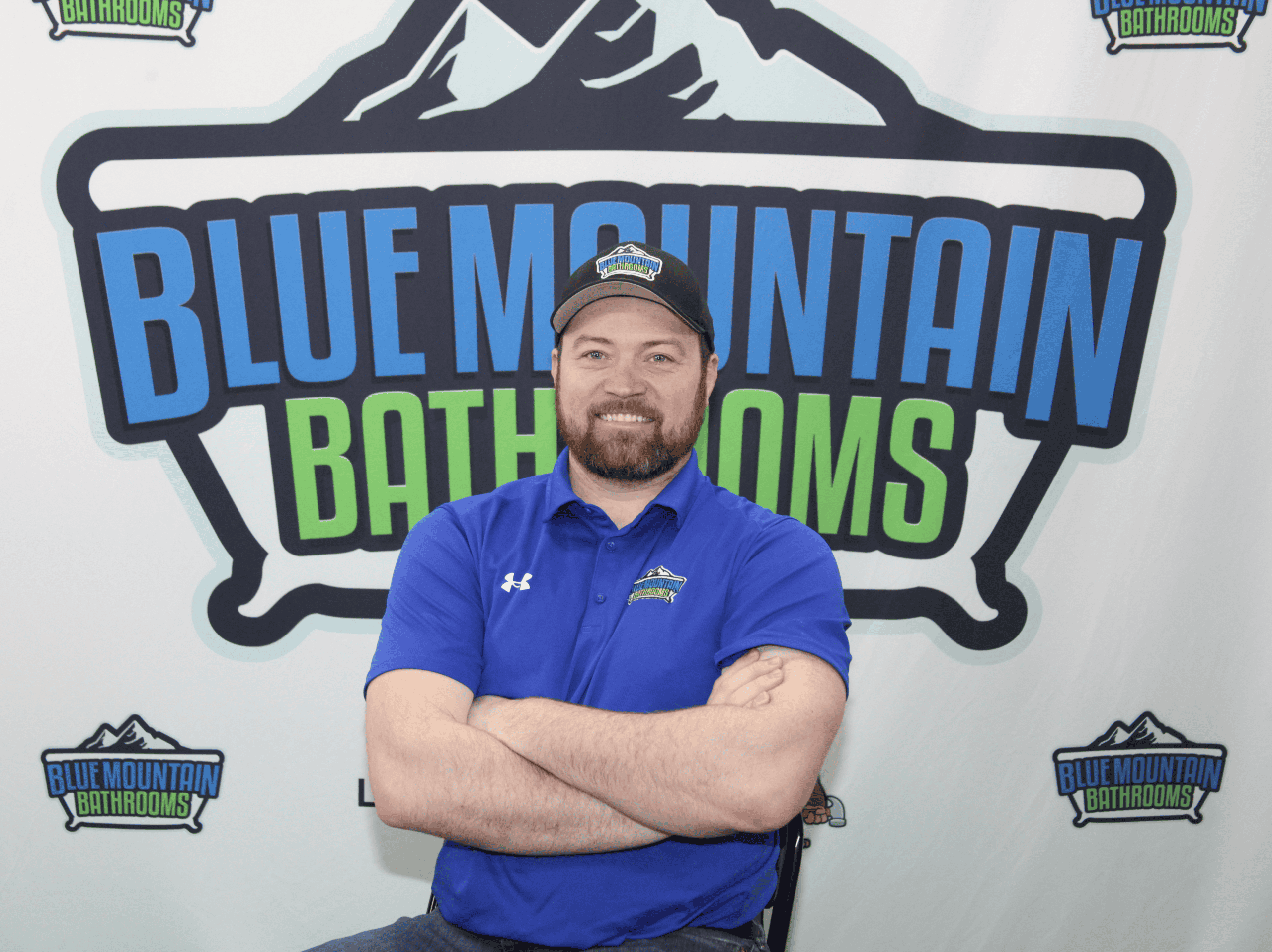 Man in blue uniform standing in front of Blue Mountain Bathrooms logo backdrop.