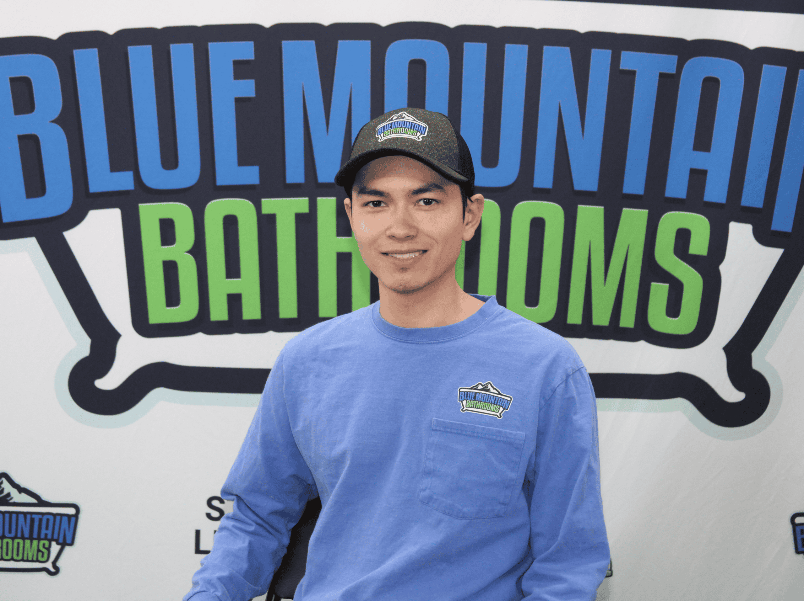 Young man in blue uniform standing in front of Blue Mountain Bathrooms logo.