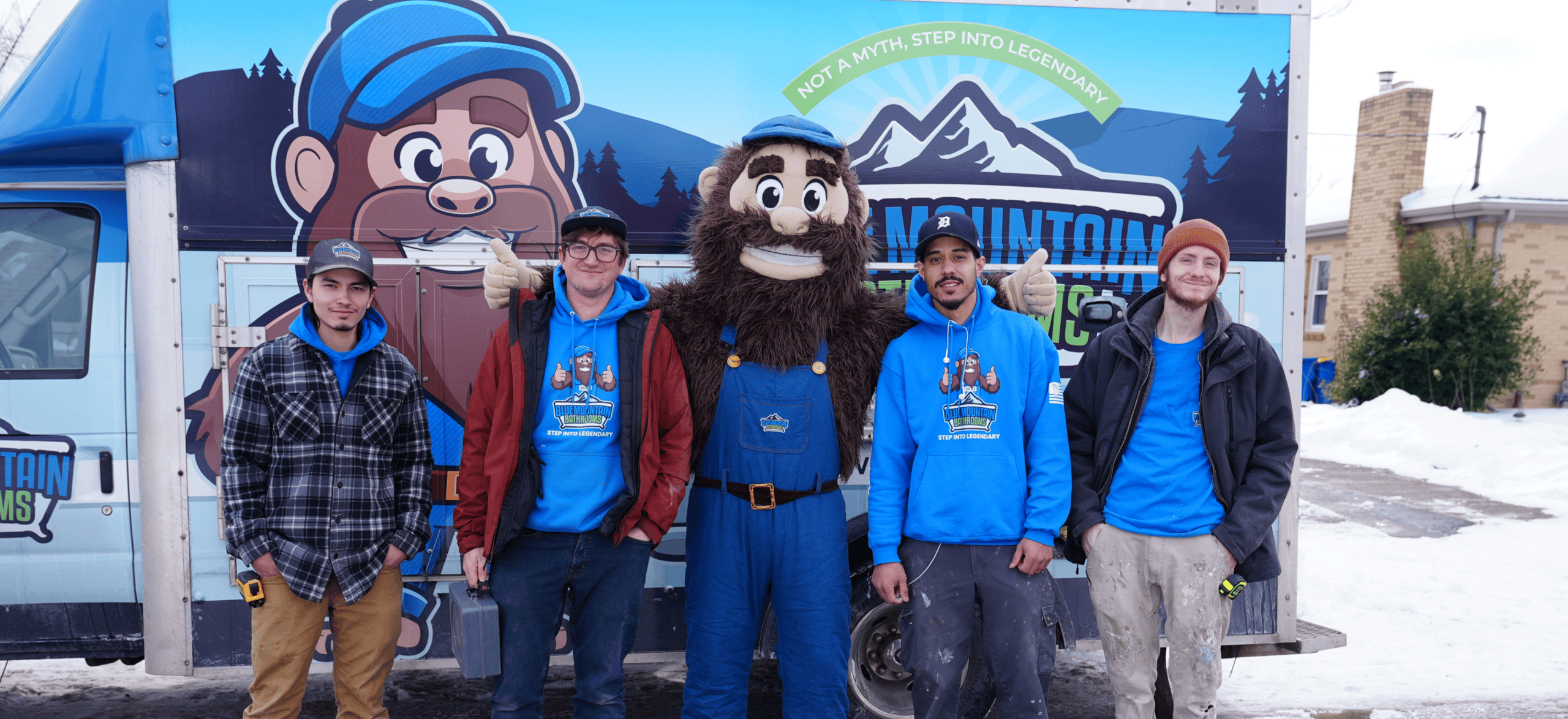 Group of four men and a mascot in front of Mountain Adventures sign, winter setting.