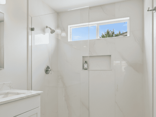 Bright modern bathroom with walk-in shower, marble walls, and a window for natural light.
