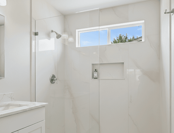 Bright modern bathroom with walk-in shower, marble walls, and a window for natural light.