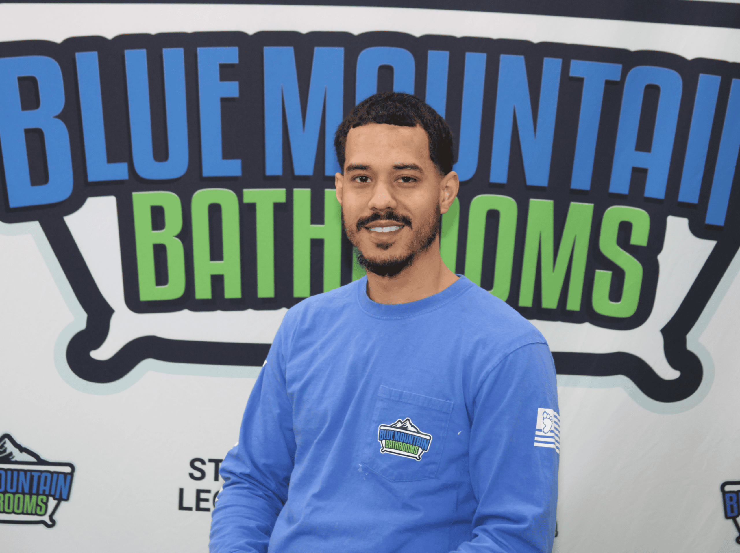 Man in blue uniform standing in front of Blue Mountain Bathrooms logo.
