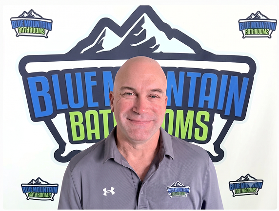 Young man in blue uniform standing in front of Blue Mountain Bathrooms logo.