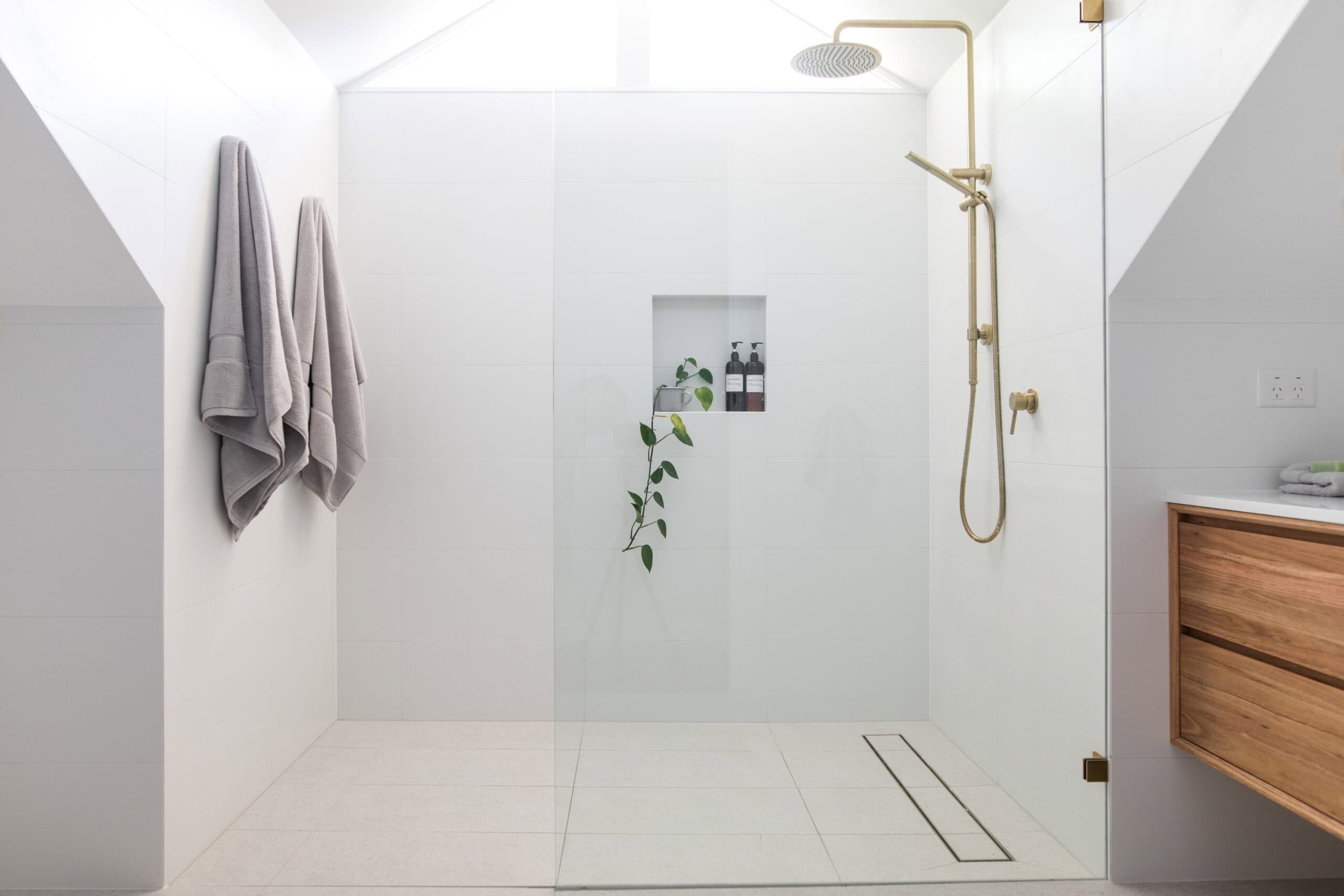 Modern walk-in shower with gold fixtures and white tiles at Blue Mountain Bathrooms.